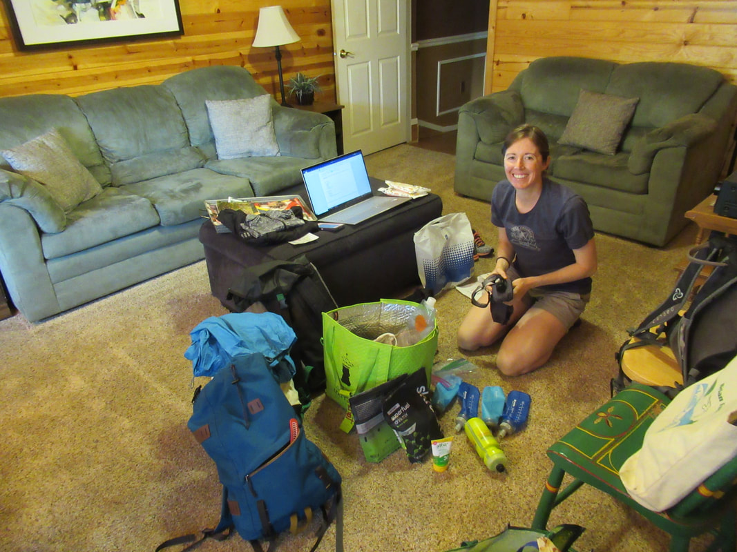 Sitting in a living room with bags, bottles, clothes and equipment spread out