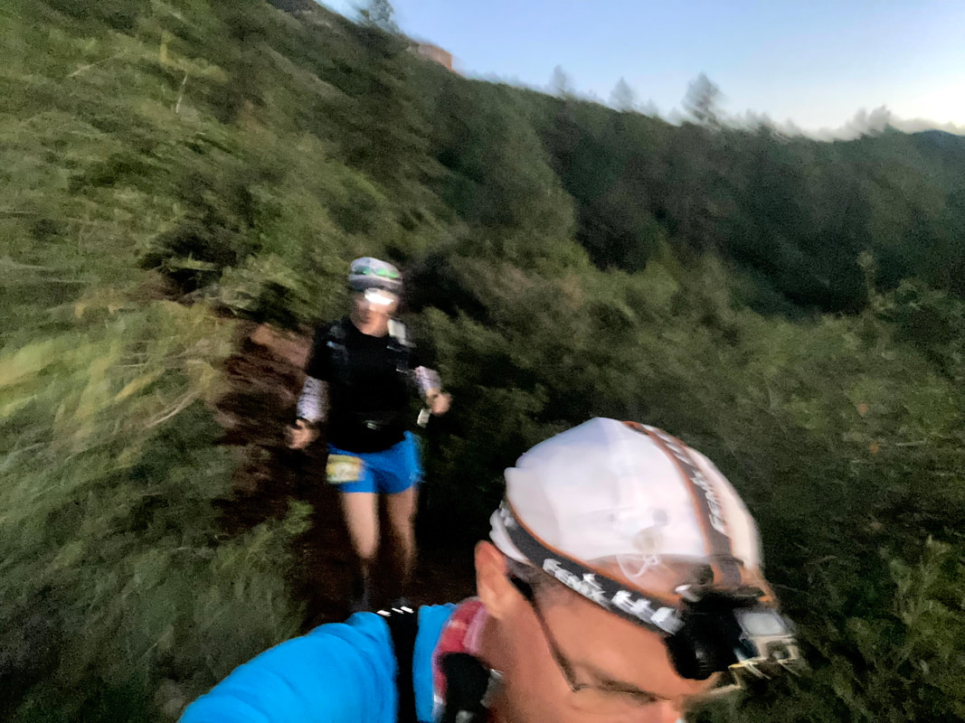 blurry photo of Kevin and Ellen running with headlamps still on but the sun coming up